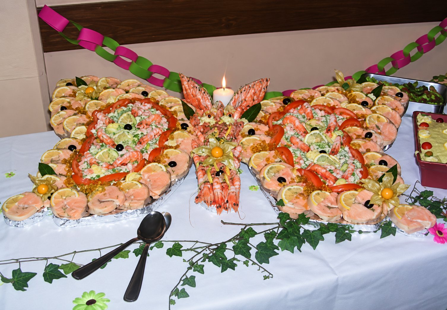 Un grand plateau de fruits de mer et de saumon disposé en forme de papillon sur une table blanche ornée de lierre, avec une bougie allumée au centre.